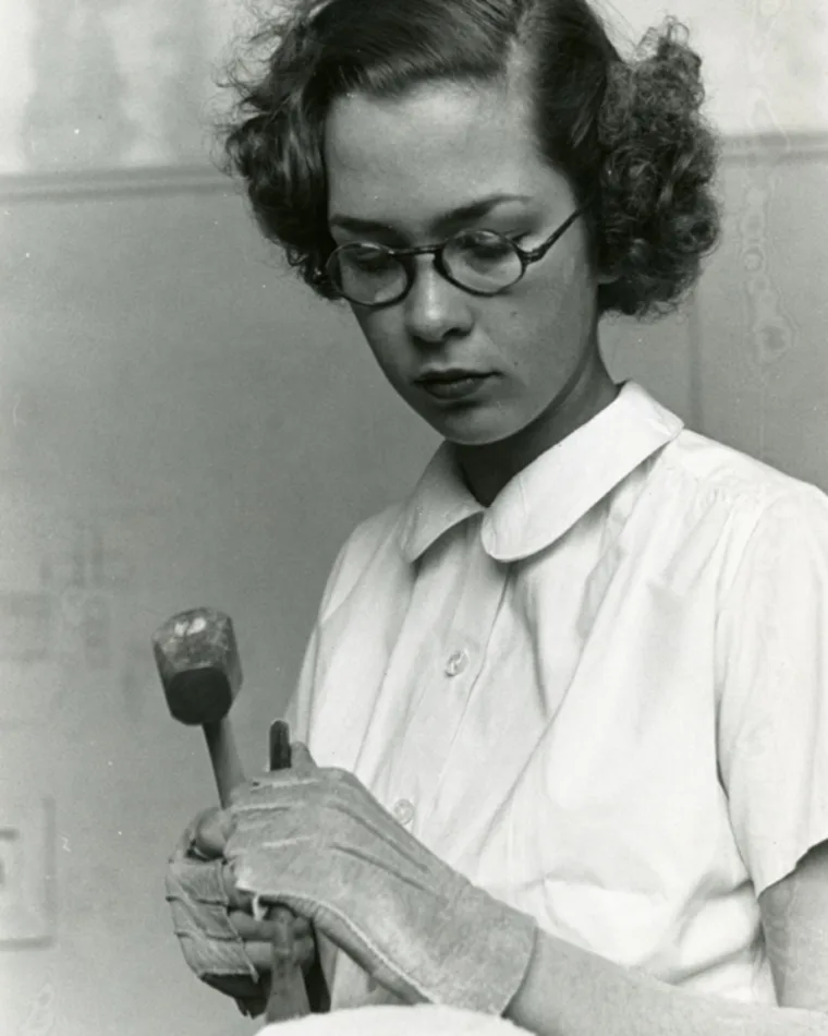 Individual focused on chiseling with hammer and eyewear, in a vintage setting.