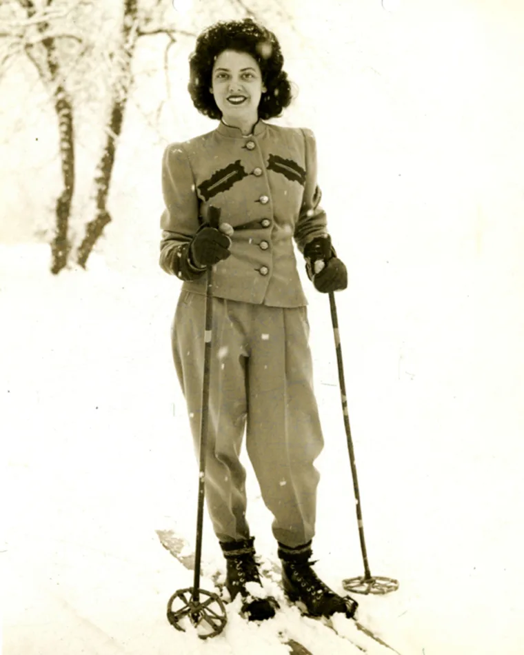 Person in vintage ski attire with poles standing in snow.