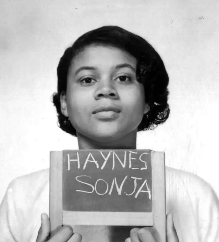 Individual holding a sign with the name "HAYNES SONJA" in front of a plain background.