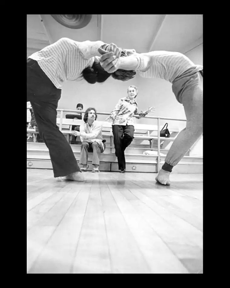 Two individuals practicing hand-to-hand combat in a gym with onlookers in the background.