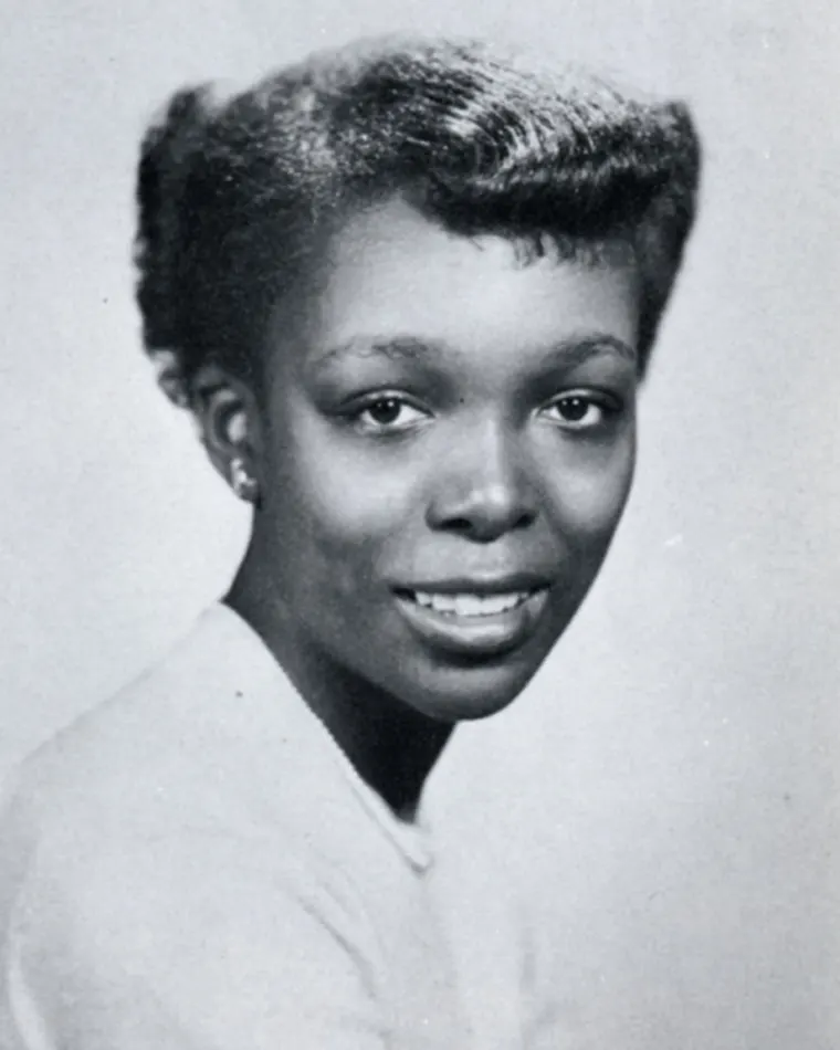 Portrait of a smiling individual with short hair, in a light-colored top. Black and white photo.