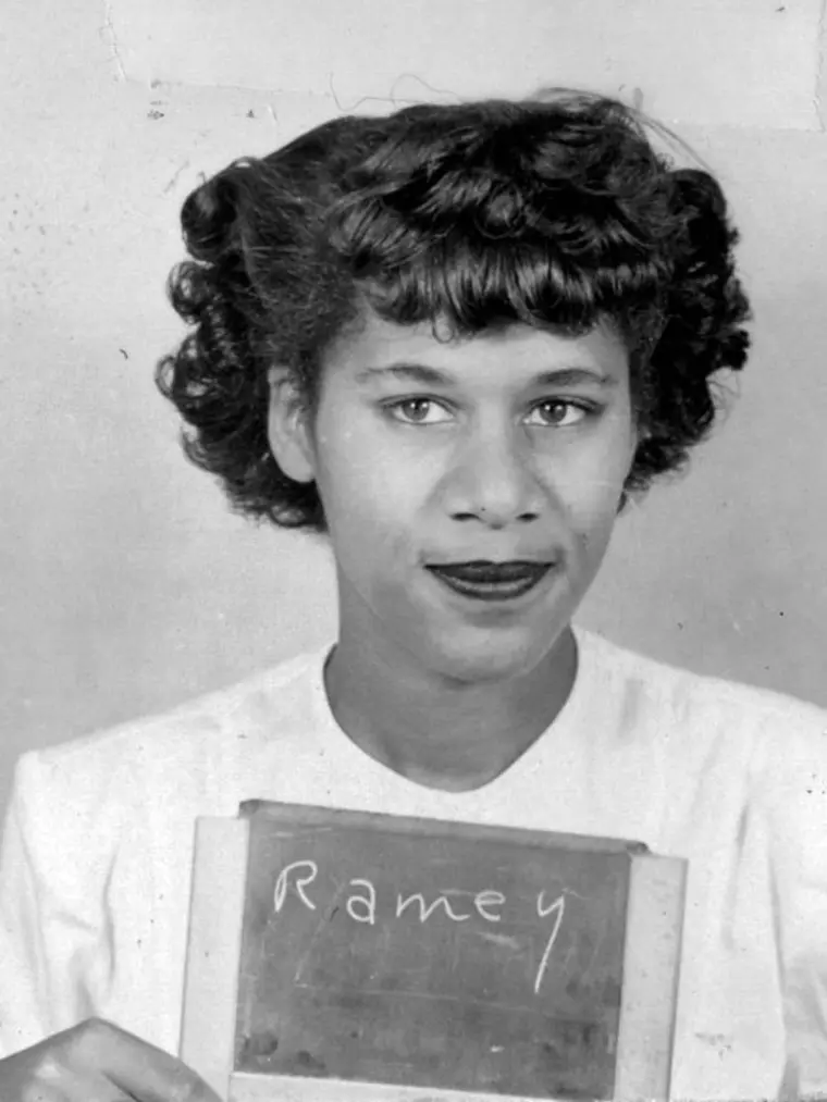 Person holding a sign with "Ramey" written on it, with curly hair and a light top.
