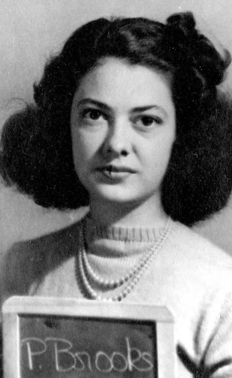 Headshot of an individual with a sweater, holding a nameplate with 'P. Brooks' written on it.