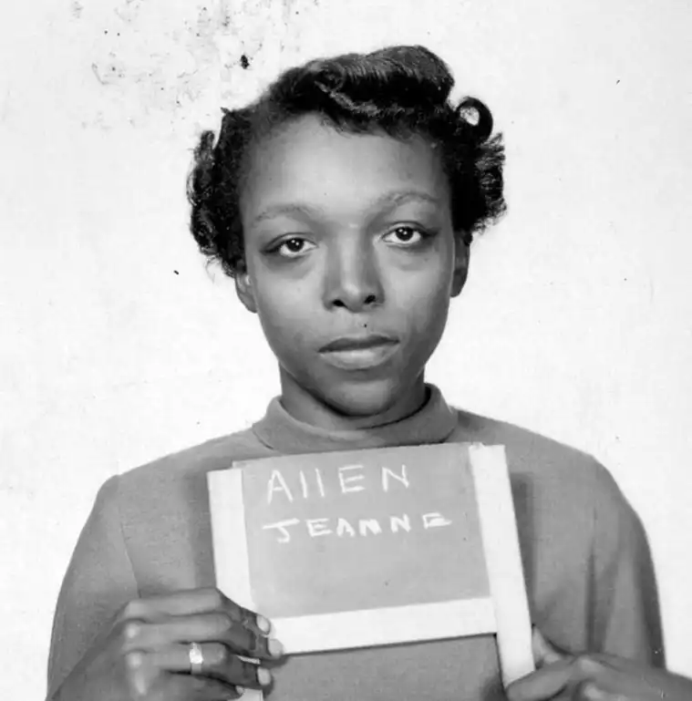 Individual holding a sign that reads "ALIEN JEANNE" in a black and white photo.