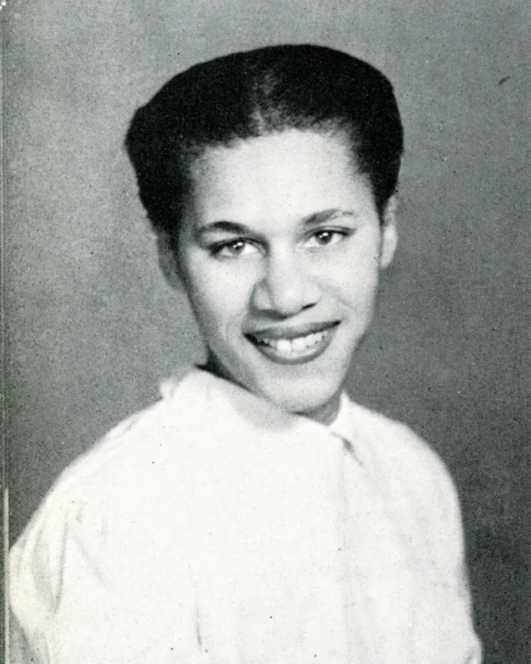 Portrait of a smiling individual with short hair against a plain background.