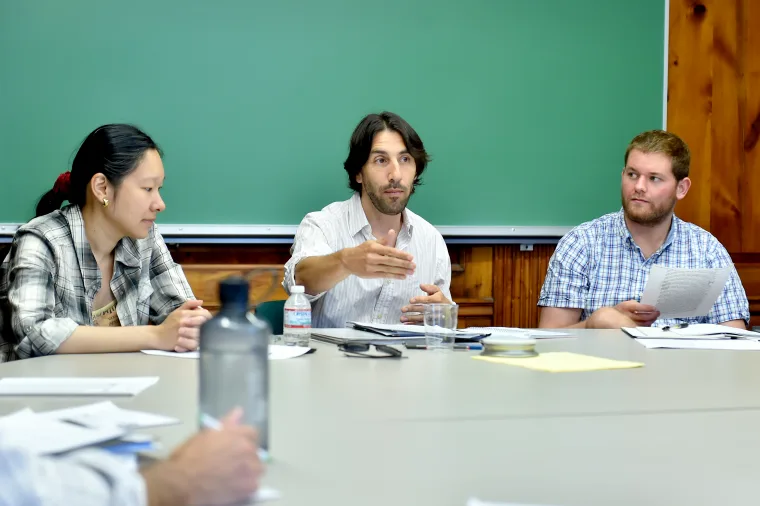 Three individuals in a meeting room with papers and water bottles on the table.