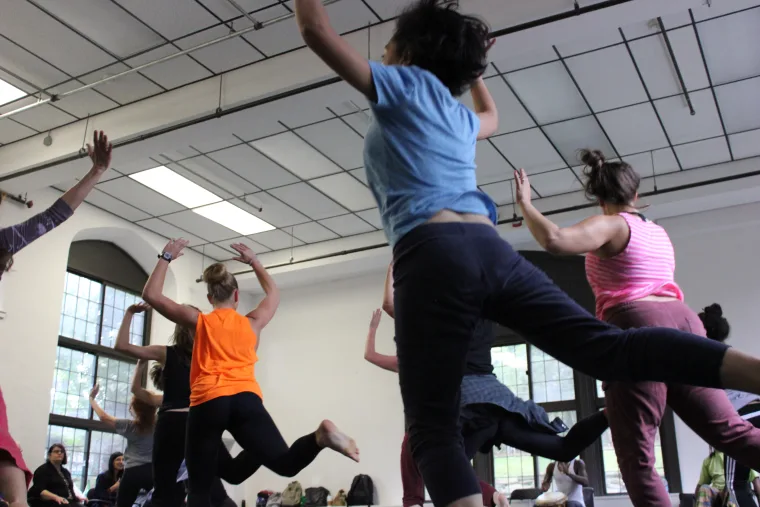 People practicing dance moves in a studio with mirrors and large windows.