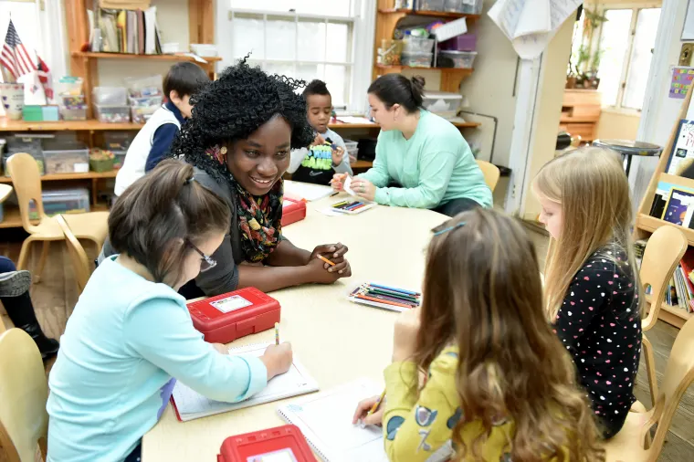 Adult and children engaged in activities around a classroom table.