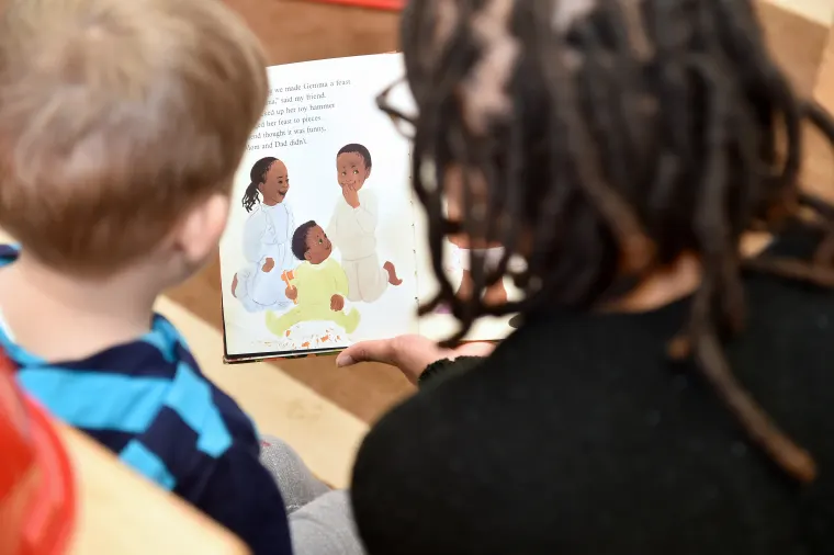 Two individuals reading a book with illustrations of children playing.
