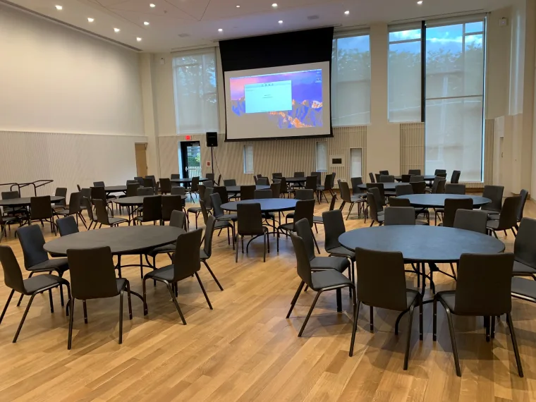 A conference room with round tables and chairs set up facing a presentation screen at the front.