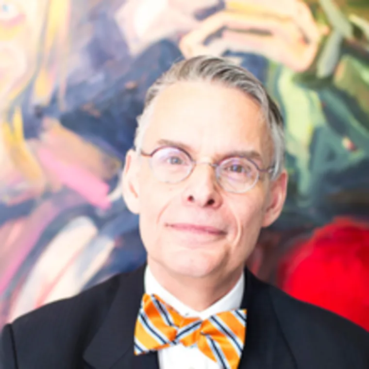 Person wearing a suit and orange-striped bow tie with a blurred colorful background.