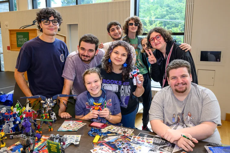 Group of people gathered around a table with action figures and comics, smiling at the camera in a bright room with large windows.