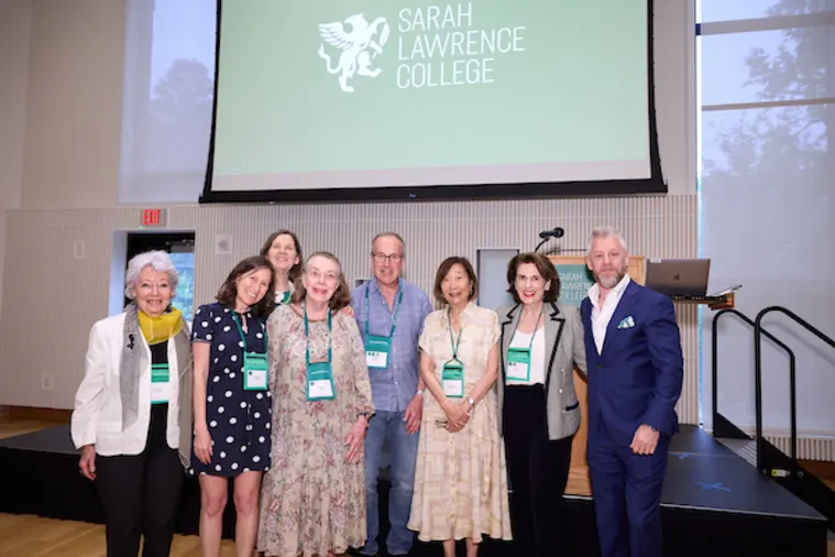 Group of people smiling on stage at Sarah Lawrence College event with a podium and screen displaying the college logo in the background.