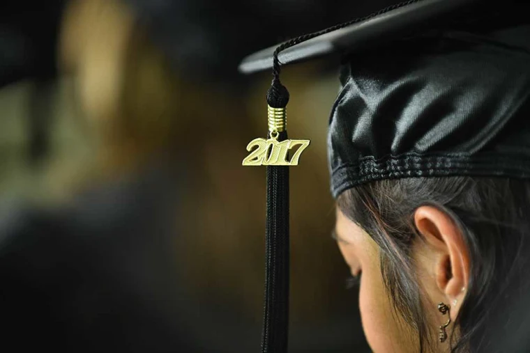 Close-up of a person wearing a graduation cap, with a tassel featuring the year "2017" and an ear with multiple piercings visible.