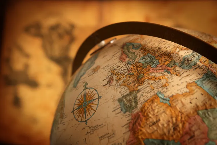 Close-up of a globe showing Europe, with a compass rose. A blurred map is in the background, creating a vintage look.
