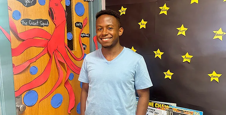 Person smiling in front of decorated classroom door with a giant squid drawing and wall with star names.