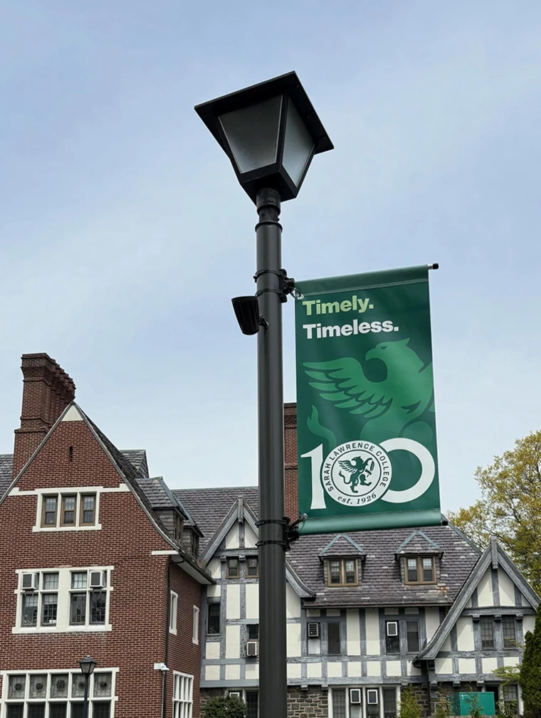 Lamp post with college anniversary banner reading "Timely. Timeless." Tudor-style building in background.