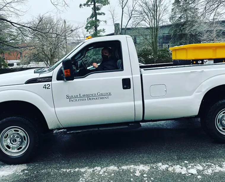 A white pickup truck with "Sarah Lawrence College Facilities Department" on the side is parked in a snowy environment.