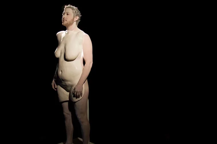 Sculpture of a person with curly hair, standing against a black background.