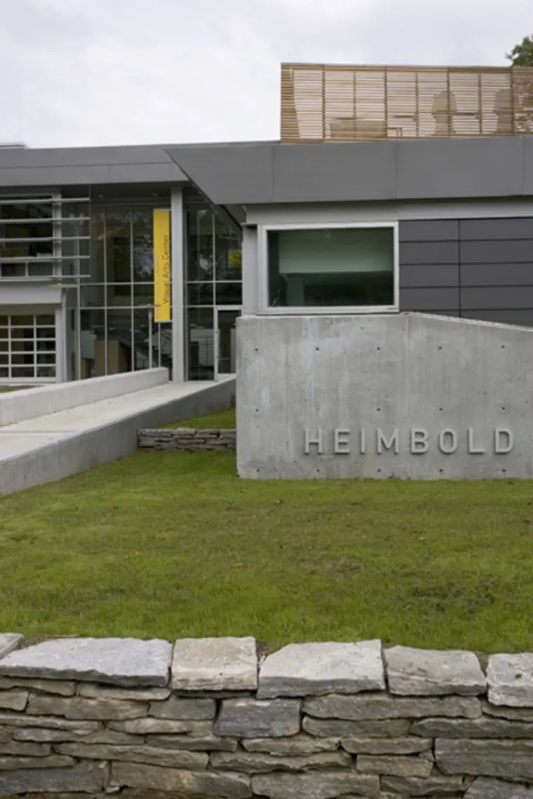 Modern building with a sign reading "Heimbold" on a concrete wall, large glass windows, and a yellow banner displaying "Visual Arts Center."