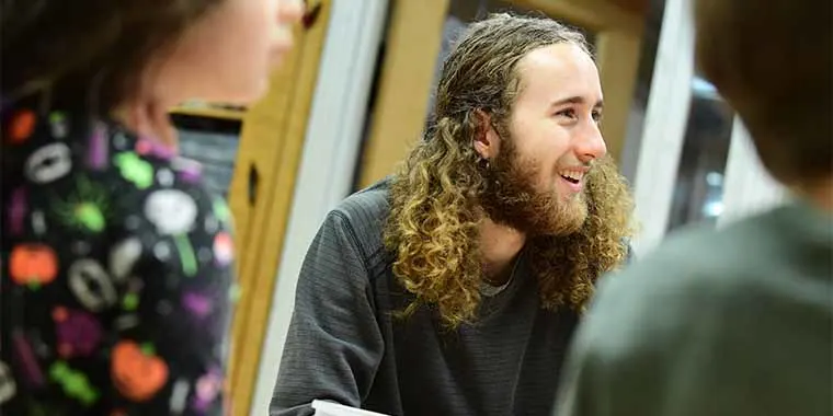 Person with long curly hair smiling, sitting at a table, interacting with others.