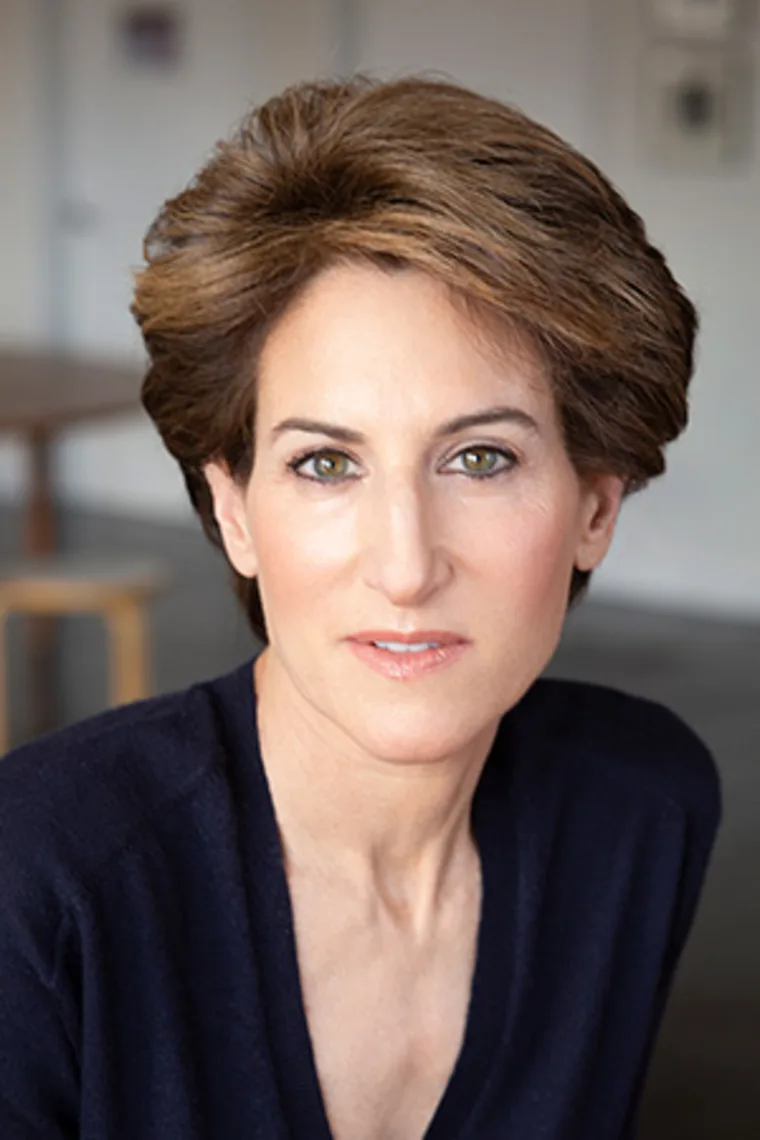 Person with short brown hair wearing a dark sweater in a softly lit room, looking directly at the camera.