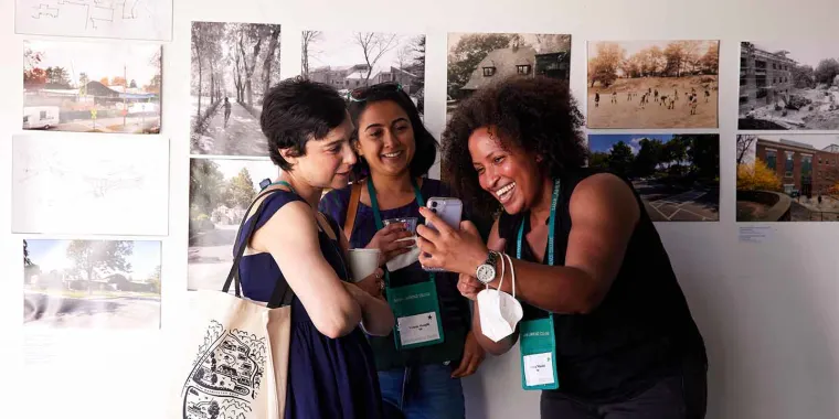 Three people smiling and looking at a smartphone in an art gallery with photo displays on the wall behind them.