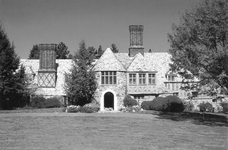 Historic stone building with a steeply pitched roof and arched entrance, surrounded by trees and grass.