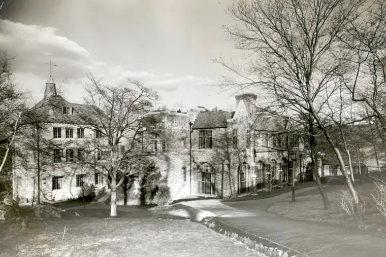 Historic brick building surrounded by leafless trees and a pathway in a grassy area, under a partly cloudy sky.
