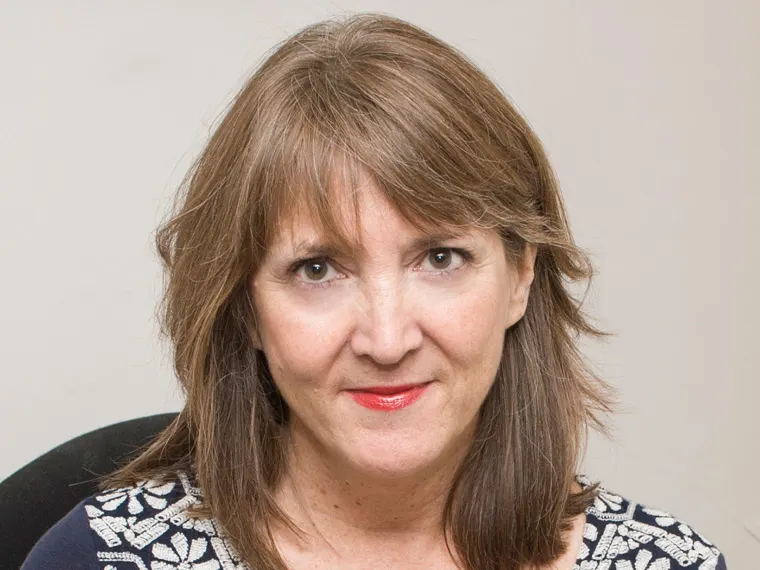 Person with shoulder-length brown hair, wearing a patterned top, looking directly at the camera with a neutral expression against a plain background.