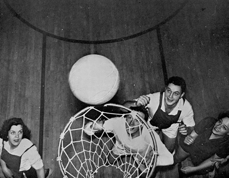 People playing basketball, viewed from above the hoop. A player attempts to shoot the ball while others watch closely around the net.