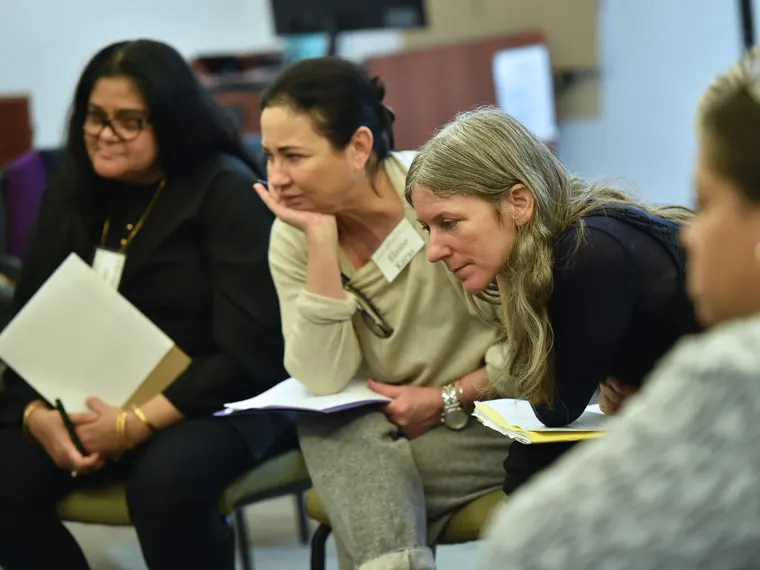 Four people sitting in a discussion, holding papers, with focused expressions in a classroom setting.