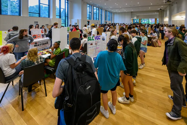 People explore various booths at a busy indoor event, with posters and tables set up in a large hall.