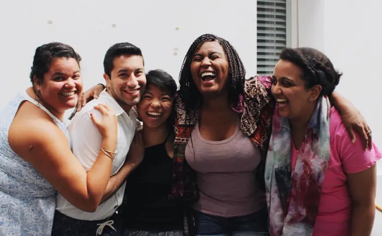 A group of five people stand closely together, smiling and laughing.