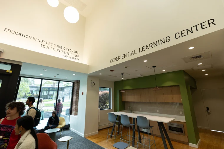 Interior of an Experiential Learning Center with several people seated and standing. The wall displays a quote by John Dewey about education.