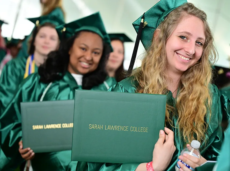 Graduates in green caps and gowns hold diplomas at Sarah Lawrence College's commencement ceremony, smiling and standing in line.