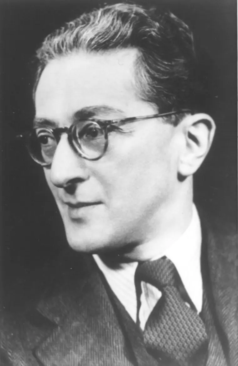 Person with glasses, wearing a suit and tie, looking to the side in a black and white portrait.