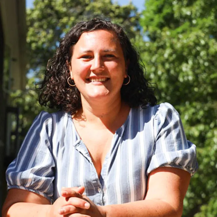 Person smiling outdoors in front of trees, wearing a striped shirt and hoop earrings.
