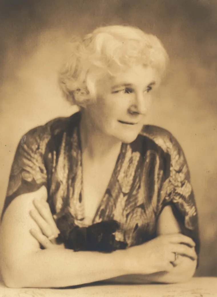 Person with curly hair sits with arms crossed, wearing a patterned top, and looks into the distance with a thoughtful expression.