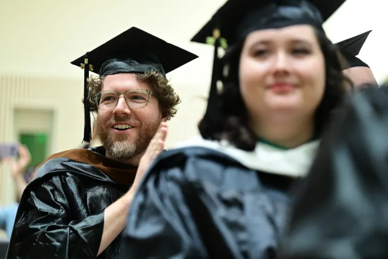 Graduates in caps and gowns smile and clap during a ceremony, seated in rows.