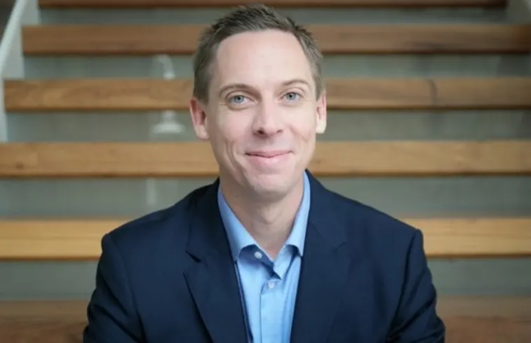Person in a blue shirt and jacket smiling while seated on wooden stairs.