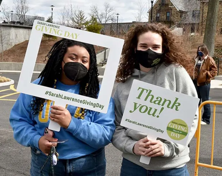 Two people wearing masks hold signs reading "Sarah Lawrence Giving Day" and "Thank you!" in an outdoor setting.