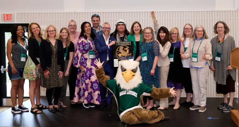Group of people smiling, holding an award plaque, with a person in a bird mascot costume posing in front.