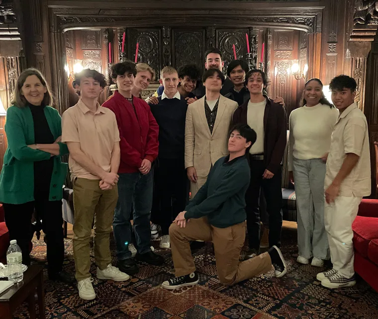 Group of people posing in a warmly lit room with ornate wooden paneling and decorative lights. Some are standing, one is kneeling.