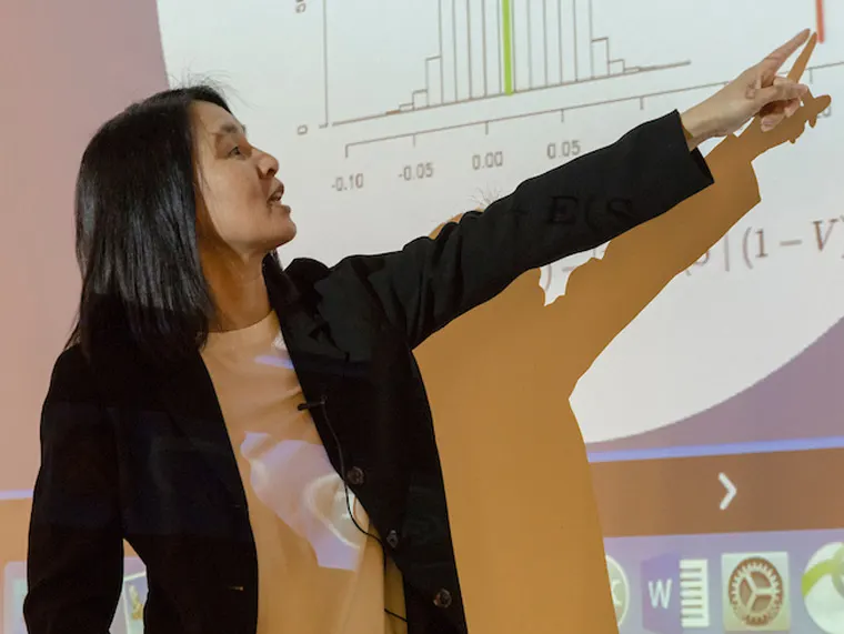 Person in a blazer pointing at a projected graph, explaining data analysis.