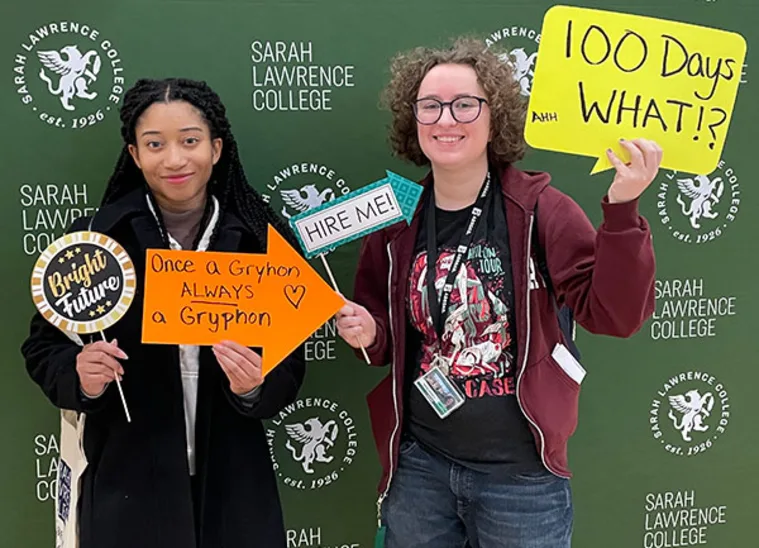 Two people in front of a Sarah Lawrence College backdrop hold signs: "Bright Future," "Once a Gryphon, Always a Gryphon," "Hire Me," "100 Days WHAT?!"
