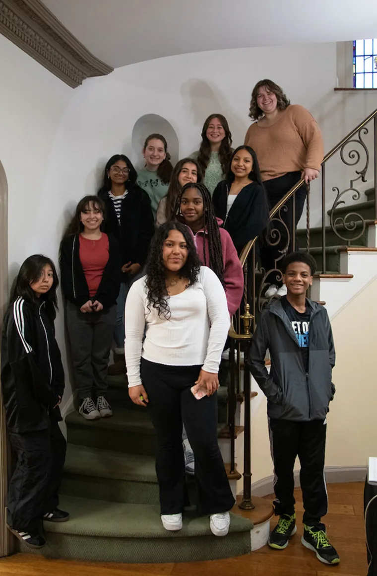 Group of people, including teenagers and adults, standing together on a curly staircase indoors, smiling at the camera.