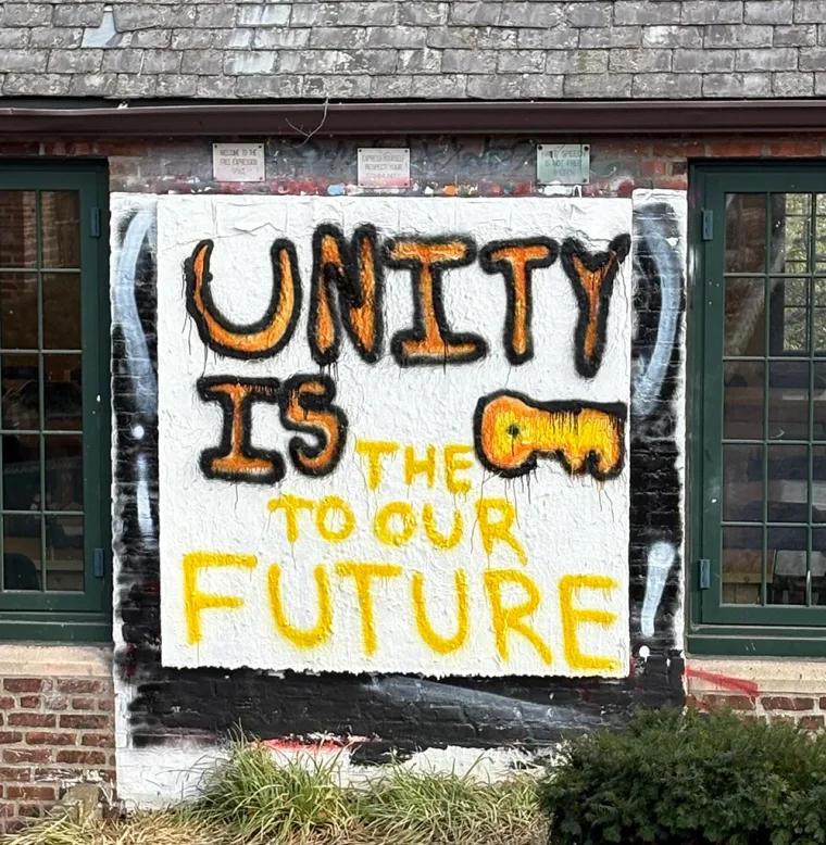 Graffiti on a brick wall reads, "UNITY IS THE KEY TO OUR FUTURE" with a painted key.