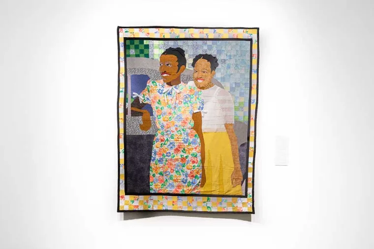Colorful quilt art depicting two smiling individuals standing together, one in a floral outfit, against a checkered background.