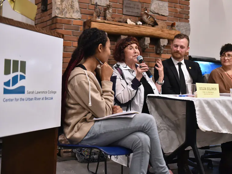 A panel discussion at Sarah Lawrence College with four speakers seated at a table, one speaking into a microphone.